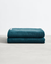 A pair of Bed Threads Aegean 100% Cotton Terry Bath Sheets is neatly stacked on a light gray surface, set against a plain white background. - view
