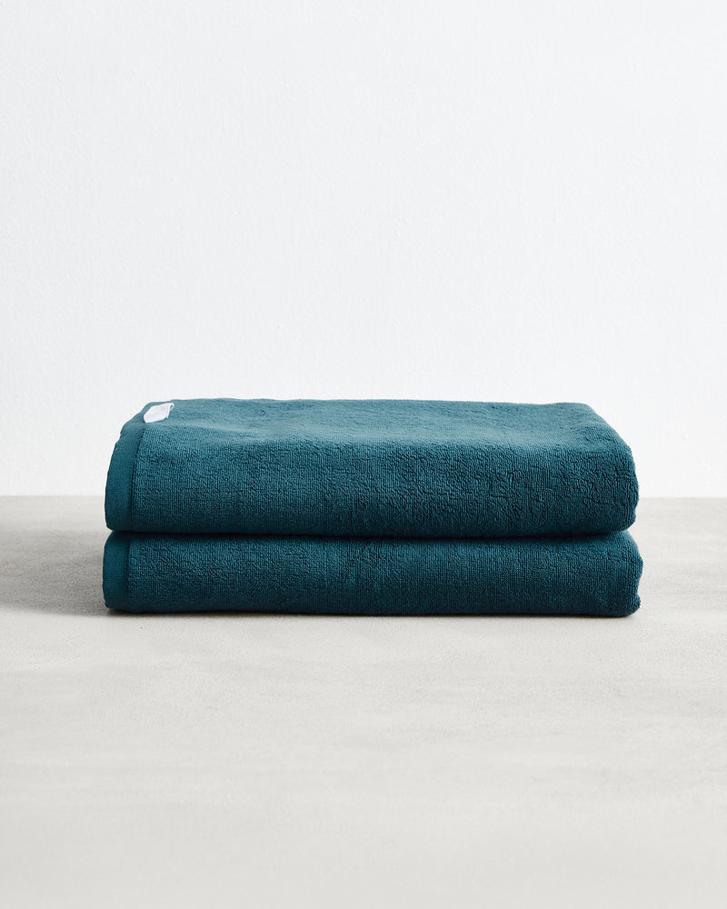 A pair of Bed Threads Aegean 100% Cotton Terry Bath Sheets is neatly stacked on a light gray surface, set against a plain white background.