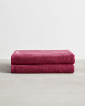 Two neatly folded Berry 100% Cotton Terry Bath Sheets by Bed Threads, stacked on a light textured surface with a white background, offering softness and high absorbency. Set of two. - view
