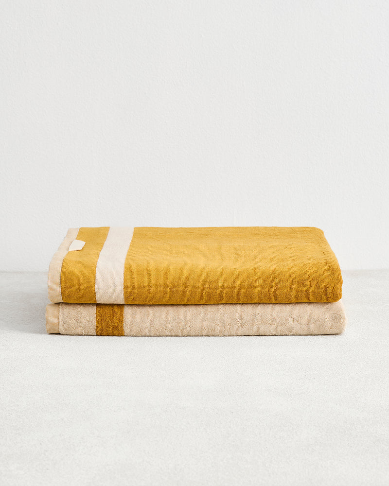The Bed Threads Crème & Turmeric Two-Toned 100% Cotton Terry Bath Sheets (Set of Two) showcase a mustard yellow towel with a white stripe and a beige towel with a mustard yellow stripe—perfect for upgrading your spa-day essentials.