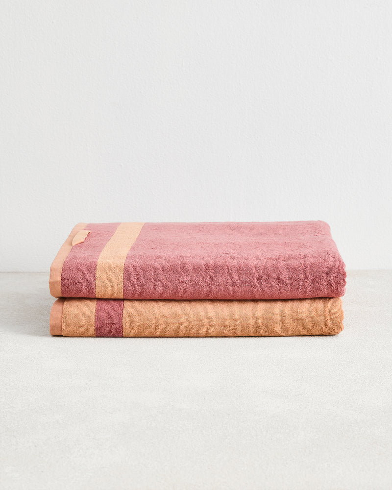 Two folded Terracotta & Pink Clay Two-Toned 100% Cotton Terry Bath Sheets by Bed Threads are stacked on a light grey surface against a white wall.