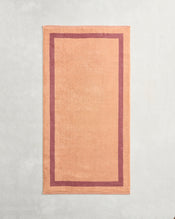 A terracotta and pink clay two-toned 100% cotton terry bath towel from Bed Threads is laid flat on a lightly textured surface. - view