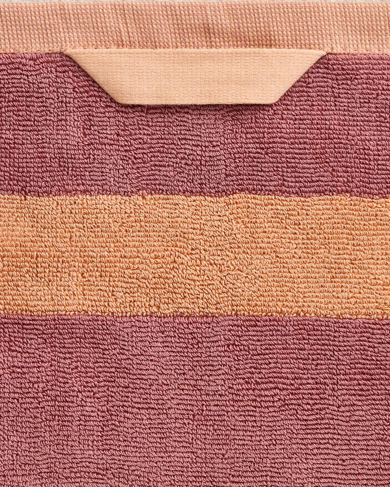 A close-up of the Bed Threads Terracotta & Pink Clay Two-Toned 100% Cotton Terry Bath Towel, crafted from 650GSM terry with a horizontal pink stripe on terracotta and finished with a color-matched hanging loop.