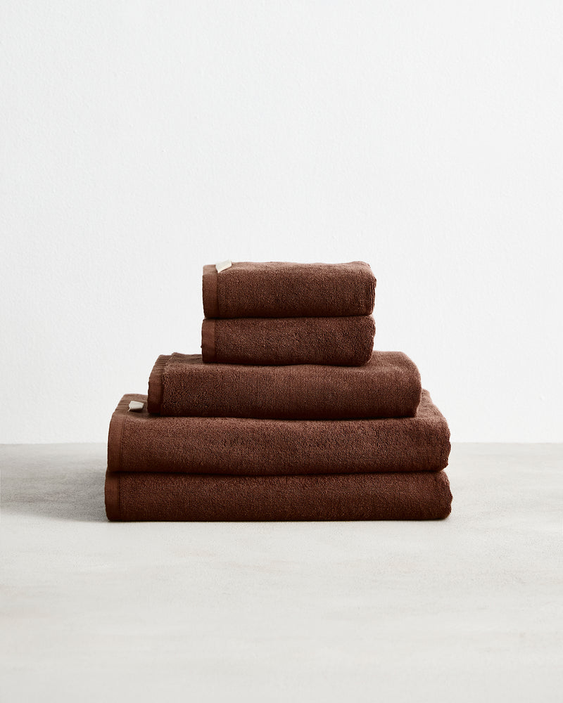 The Bed Threads Espresso 100% Cotton Terry Bath Towel Bundle, featuring neatly stacked towels in various sizes, is displayed on a light surface against a plain white background.