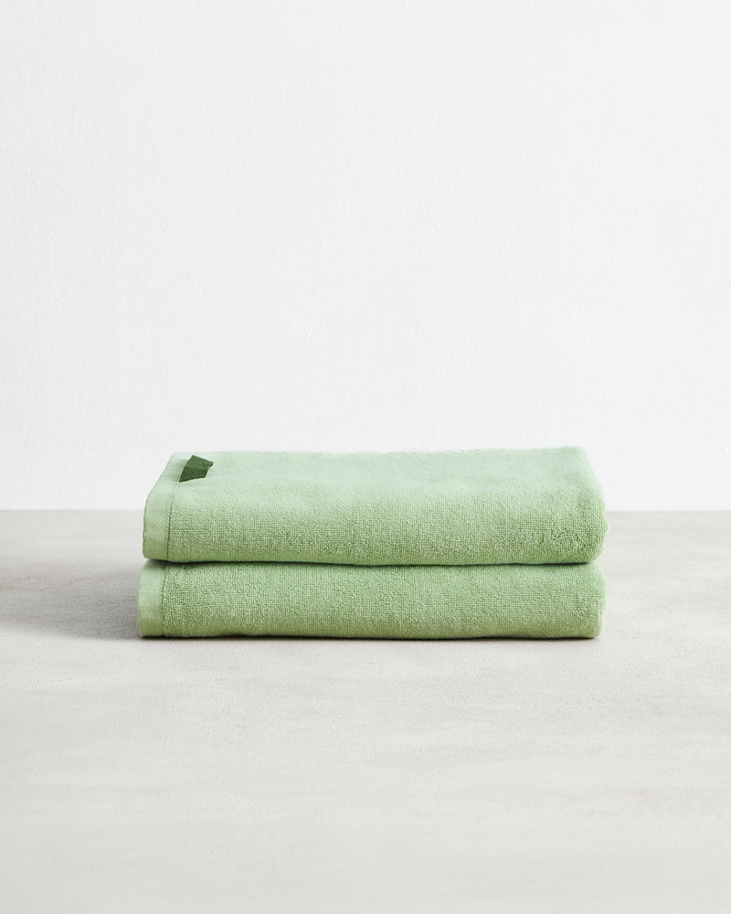 The Apple 100% Cotton Terry Bath Towels (Set of Two) by Bed Threads are stacked neatly on a smooth, light surface with a plain white background, highlighting their absorbency and quality.