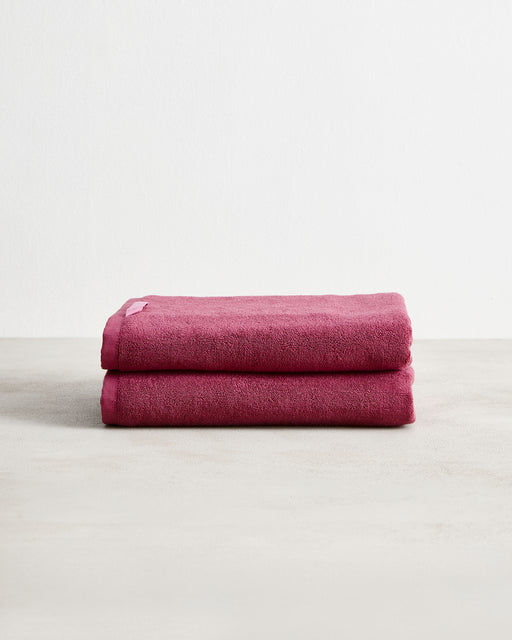 Two Berry 100% Cotton Terry Bath Towels by Bed Threads, neatly folded and stacked, shown against a plain white background. Set of two in a rich dark pink shade on a light-colored surface.