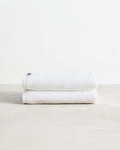 The Bed Threads Crisp White 100% Cotton Terry Bath Towels (Set of Two) are neatly folded and stacked on a smooth surface, with a plain white background highlighting their plush absorbency. - view