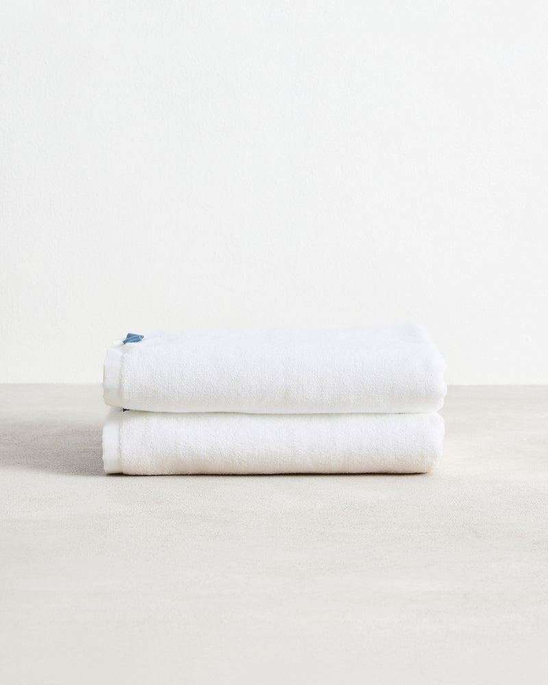 The Bed Threads Crisp White 100% Cotton Terry Bath Towels (Set of Two) are neatly folded and stacked on a smooth surface, with a plain white background highlighting their plush absorbency.