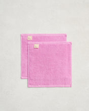 Two Bubblegum 100% Cotton Terry Face Washers by Bed Threads are displayed on a light gray surface, slightly overlapping. Their soft, absorbent terry fabric is gentle on skin. Set includes two rectangular pink face washers with light pink tags. - view