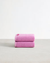 Two neatly folded Bubblegum 100% Cotton Terry Hand Towels by Bed Threads are stacked on a light gray surface with a plain white background. This highly absorbent set of two adds comfort and style to your daily routine. - view