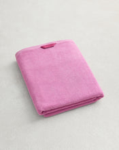 A Bubblegum 100% Cotton Terry Bath Sheet by Bed Threads, plush and quick-drying, with a small rectangular tag, sits neatly folded on a light-colored textured surface. - view