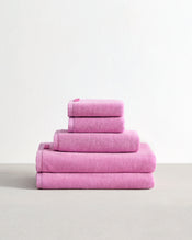 The Bed Threads Bubblegum 100% Cotton Terry Bath Sheet Bundle features four absorbent pink towels in assorted sizes, neatly stacked on a light surface against a plain white background. - view