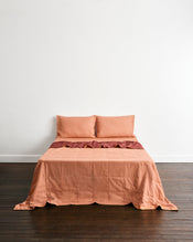 A bed dressed in a muted peach-orange quilt cover in Cacao & Hazelnut with two matching pillowcases in Hazelnut, set against a plain white wall and dark wood floor. - view