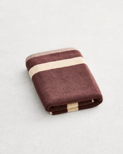 A folded cotton terry bath mat on a grey background, in a cacao colourway with a creme border.  - view