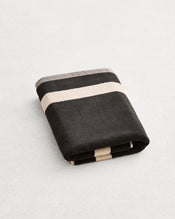 A folded cotton terry bath mat on a grey background, in a charcoal colourway with an oatmeal border. . - view