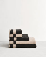 Stack of cotton terry towels in reversible colours oatmeal and charcoal. - view