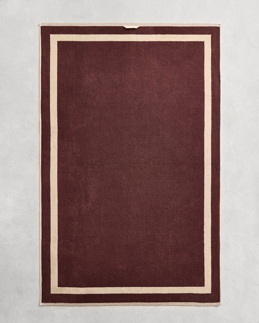 Flat cotton terry bath sheet on a grey background in a cacao colour with a creme border.