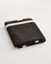 A folded cotton terry bath sheet on a grey background, in a charcoal colourway with an oatmeal border. - view