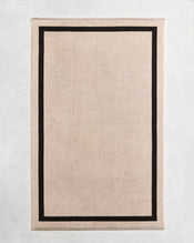 Flat cotton terry bath towel on a grey background in an oatmeal colour with a charcoal border. - view