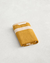 The Bed Threads Crème & Turmeric Two-Toned 100% Cotton Terry Hand Towel, crafted from plush 650GSM terry, is neatly folded and rests on a light textured surface. - view