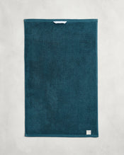 The Bed Threads Aegean 100% Cotton Terry Hand Towel (650GSM) in teal is shown flat on a light gray surface, featuring a small white label in one corner and a central hanging loop. Quick-drying and stylish for easy access. - view