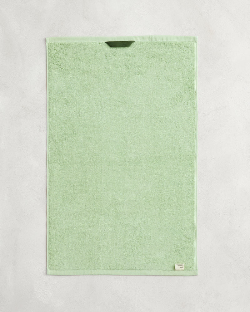 A set of two Apple 100% Cotton Terry Hand Towels by Bed Threads, in light green, are neatly displayed on a textured surface. Featuring a small corner label, these stylish towels are highly absorbent and functional.