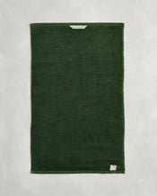 A set of two Moss 100% Cotton Terry Hand Towels by Bed Threads is shown flat on a light gray surface, featuring a small light green loop near one edge and a white label in one corner. - view