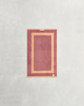 The Bed Threads Terracotta & Pink Clay Two-Toned 100% Cotton Terry Hand Towel, made from plush 650GSM quick-drying terry, features a lighter pink border, small fabric loop, and tag at the bottom corner. - view