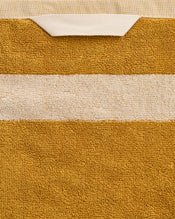A close-up of the Bed Threads Crème & Turmeric Two-Toned 100% Cotton Terry Hand Towel, made from plush 650GSM terry, featuring a beige stripe and fabric loop, set against a textured background. Comes as a set of two. - view