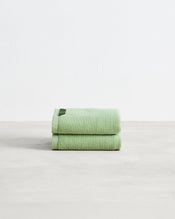 Two light green Apple 100% Cotton Terry Hand Towels by Bed Threads are neatly folded and stacked on a smooth, light surface with a plain white background. - view