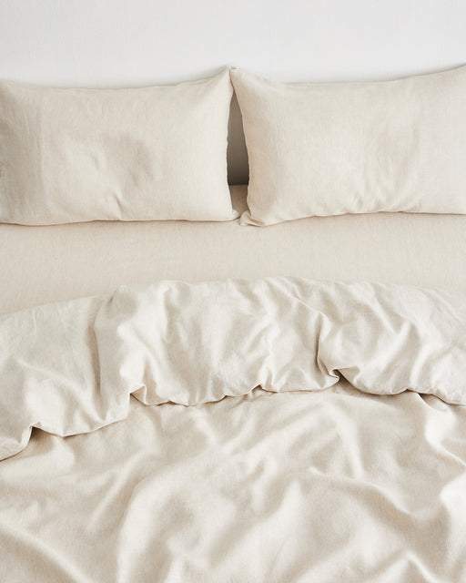 Two Bed Threads Oatmeal & White Stripe 100% French Flax Linen Pillowcases (Set of Two) are arranged on a bed with a matching crumpled duvet and light sheet, creating a simple, cozy look.