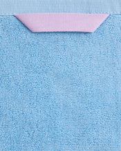 Close-up of the Bed Threads Sky 100% Cotton Terry Hand Towel (650GSM) in light blue, with a small folded pink tab at the top edge, set against a matching light blue background. - view