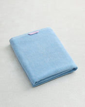 The Bed Threads Sky 100% Cotton Terry Bath Sheet, folded neatly with a small pink label, rests on a light, textured surface. - view