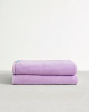 Two neatly folded, light purple towels stacked on a smooth, light gray surface with a plain white wall in the background. - view