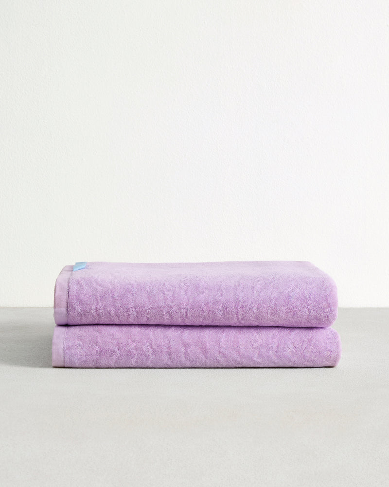Two neatly folded, light purple towels stacked on a smooth, light gray surface with a plain white wall in the background.