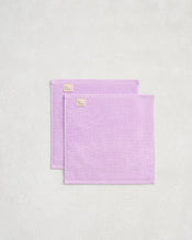The Bed Threads Violet 100% Cotton Terry Face Washers (Set of Two) are neatly folded on a textured surface, highlighting their absorbent, skin-friendly terry fabric and subtle beige tags. - view