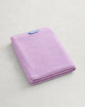The Bed Threads Violet 100% Cotton Terry Bath Sheet, neatly folded with a blue label, rests on a light textured surface, showcasing the elegance and quality of premium cotton. - view