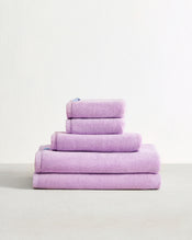 The Bed Threads Violet 100% Cotton Terry Bath Sheet Bundle, featuring five highly absorbent towels in varying sizes, is neatly stacked on a light surface against a plain white background. - view