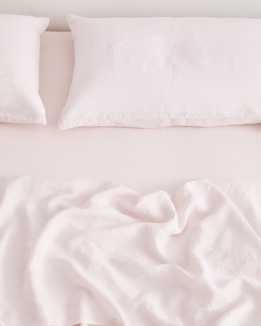 A neatly made bed with two pillows and a lightly wrinkled Rosewater 100% French Flax Linen Fitted Sheet, viewed from above against a white wall—showcasing premium, temperature-regulating bedding.