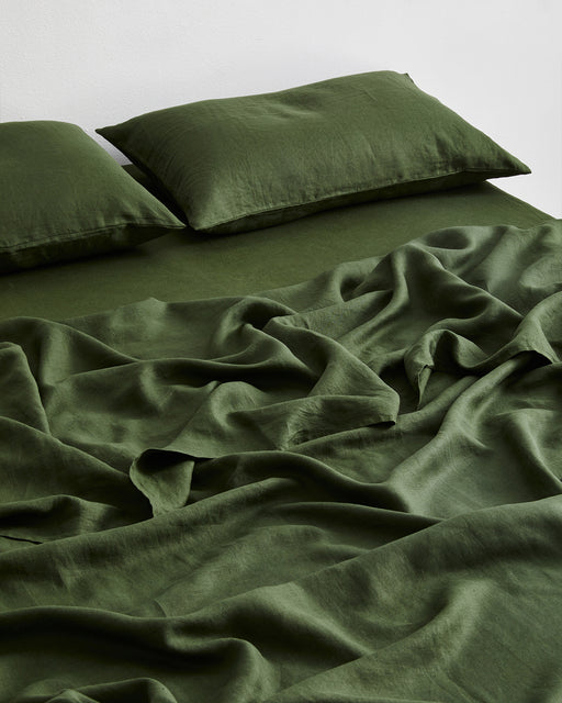 A neatly made bed with two pillows, all dressed in the Bed Threads Olive 100% French Flax Linen Flat Sheet. The slightly rumpled blanket enhances the cozy, inviting look.