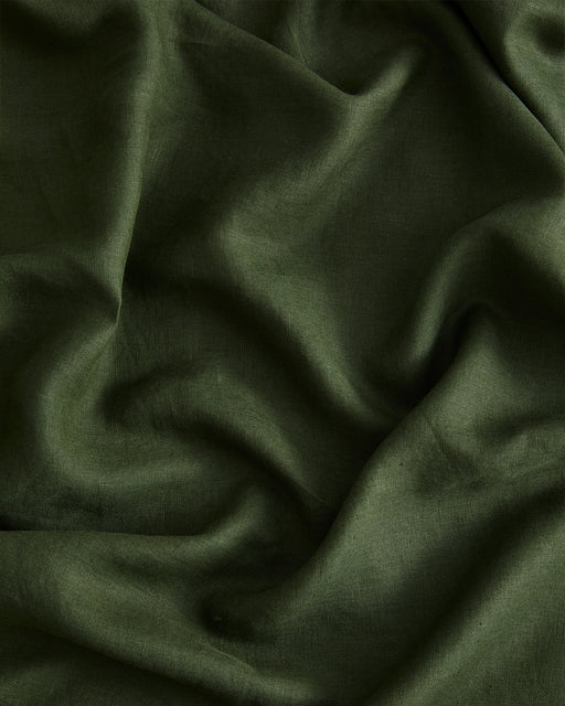 A close-up of the Olive 100% French Flax Linen Flat Sheet by Bed Threads reveals its dark green hue, smooth yet slightly textured surface, and soft, natural folds and creases.
