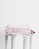 A neatly folded Bed Threads Rosewater 100% French Flax Linen Sheet Set rests on a glossy white stool against a plain white background.