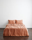 A neatly made bed features the Bed Threads Hazelnut 100% French Flax Linen Bedding Set—duvet cover and two matching pillows—set against a plain white wall and a dark wooden floor.